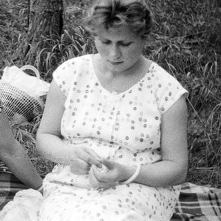 Here's a brief summary of the image: Woman and girl seated outdoors, possibly on a picnic blanket.