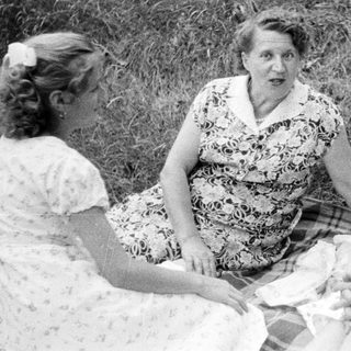 Three women sit on a blanket outdoors.
