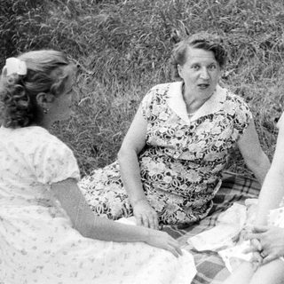Three women sit on a blanket outdoors.