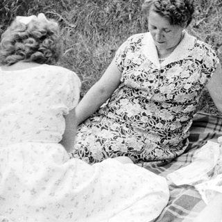 Three women sitting on a blanket in a field.