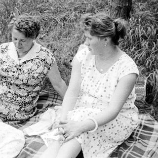 Three women sitting on a blanket in a field.