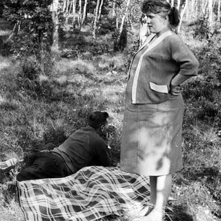 Couple relaxing outdoors on a blanket in a wooded area.