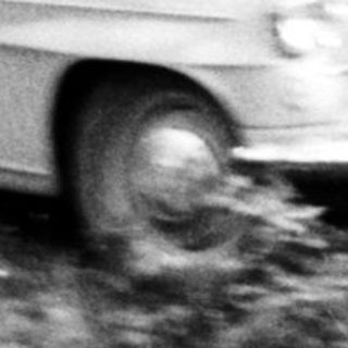 Woman stands near a vintage car in a wooded area.