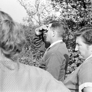 Three people standing outdoors, viewing something in the distance.