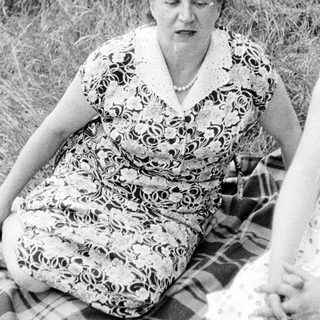 Woman in patterned dress sits on blanket in grass.