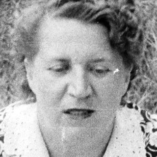 Woman in patterned dress sits on blanket in grass.