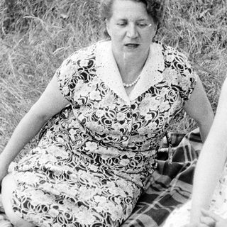 Woman in patterned dress sits on blanket in grass.