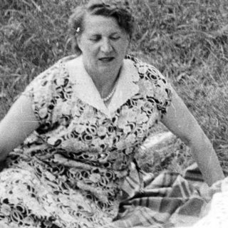 Three people sitting on a blanket outdoors in a field.