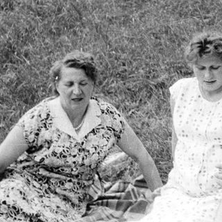 Three people sitting on a blanket outdoors in a field.