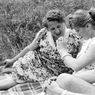 Here's a brief summary of the image: Three people relaxing on a blanket in a grassy area.