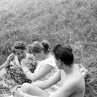 Here's a brief summary of the image: Three people relaxing on a blanket in a grassy area.