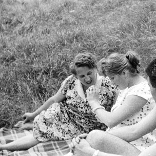 Here's a brief summary of the image: Three people relaxing on a blanket in a grassy area.