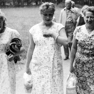 Black and white photo of women walking outdoors with baskets.