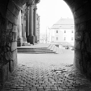 Stone archway frames a view of a building and plaza.