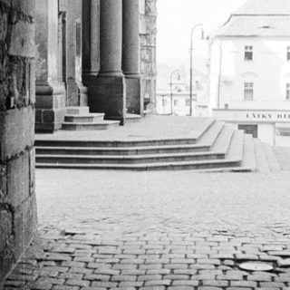 Stone archway frames a view of a building and plaza.