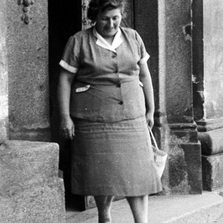Woman in vintage dress stands on stone steps.