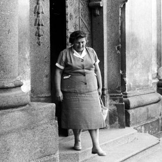 Woman in vintage dress stands on stone steps.