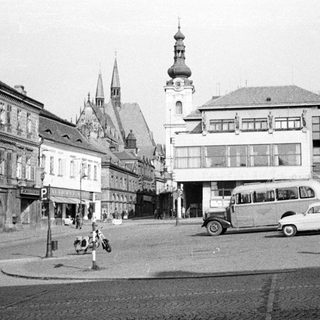 Black and white photo of a town square with vehicles.