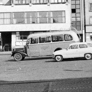 Black and white photo of a town square with vehicles.