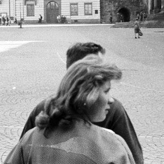 People walk through a cobblestone square with historic buildings.
