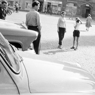 People stand and walk near a vintage car on a street.