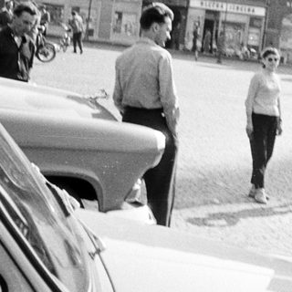People stand and walk near a vintage car on a street.