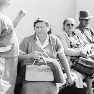 Here's a brief summary of the image: Group of people seated, appearing to wait somewhere.