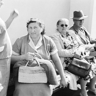 Here's a brief summary of the image: Group of people seated, appearing to wait somewhere.