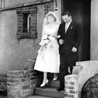 Bride and groom exit building, bird in ornate cage.