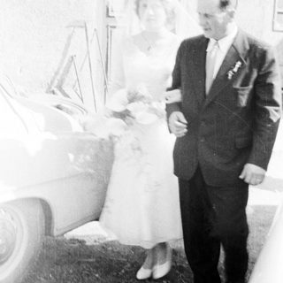 Couple poses near a car on their wedding day.