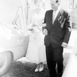 Couple poses near a car on their wedding day.