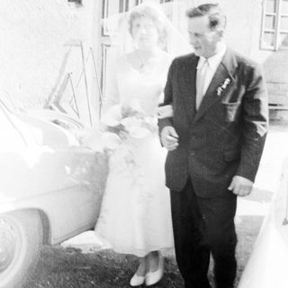 Couple poses near a car on their wedding day.