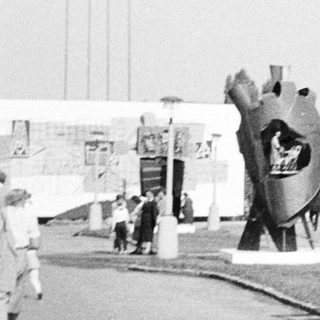 Sculptures, building, and people at an outdoor exposition.