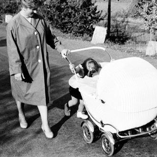 Woman pushes a baby in an ornate vintage pram.