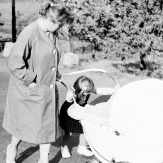 Woman stands near a vintage baby carriage on a path.