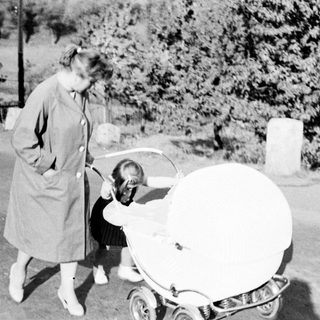 Woman stands near a vintage baby carriage on a path.