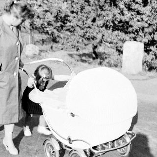 Woman stands near a vintage baby carriage on a path.