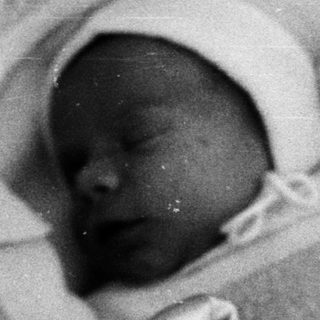 Black and white image of a baby sleeping in a crib.