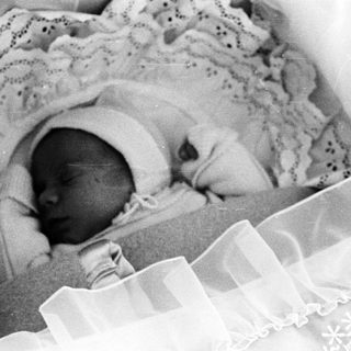 Black and white image of a baby sleeping in a crib.