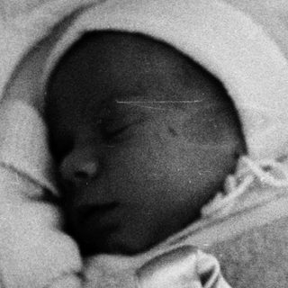 Black and white image of a baby sleeping in a crib.