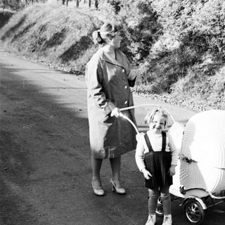 Woman and child with unusual wicker stroller on a road.