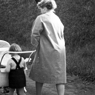 Woman walks along a road, pushing a baby carriage.