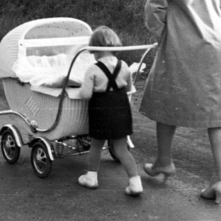 Woman walks along a road, pushing a baby carriage.
