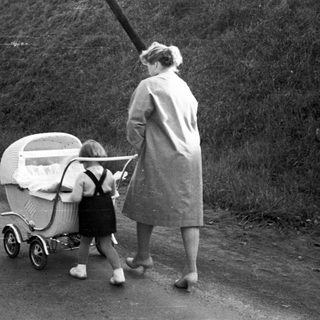 Woman walks along a road, pushing a baby carriage.