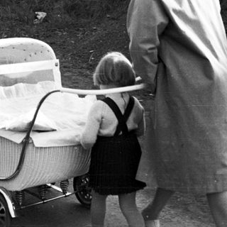 Woman and child near a vintage wicker baby carriage.