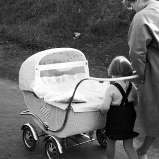 Woman and child near a vintage wicker baby carriage.