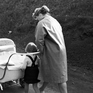 Woman and child near a vintage wicker baby carriage.
