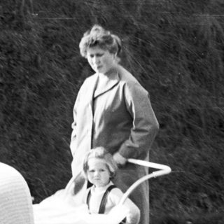 Woman pushes a wicker baby carriage along a road.