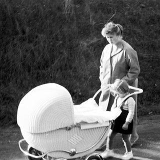 Woman pushing a vintage wicker baby carriage outdoors.