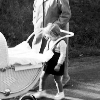 Woman pushing a vintage wicker baby carriage outdoors.